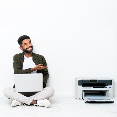 A Man Sitting on the Floor Next to a Printer, Utilizing the Service to Print Checks Free.