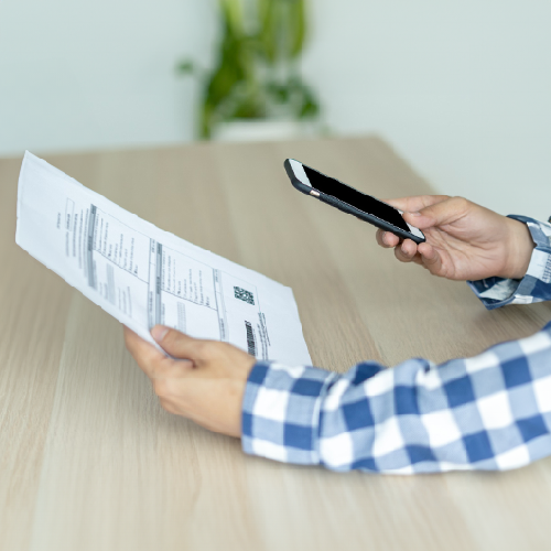 A Person Holds a Mobile Phone and a Bill. They Use a Bill Pay Service to Pay the Bill