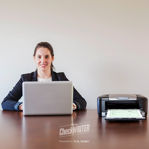 A Professional Woman Seated at a Desk, Using a Laptop with Check Printing Software Free on the Screen, and a Printer Beside Her