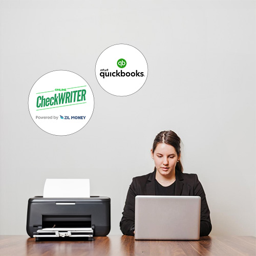 Checks For QuickBooks – Users Can Print Check More Easily A Woman Sits at a Desk Using a Laptop with Checks For QuickBooks Printing Using a Printer, a Logo on the Wall Behind Indicates QuickBooks